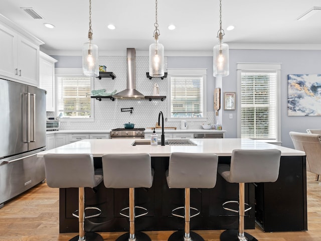 kitchen featuring white cabinetry, an island with sink, premium appliances, a breakfast bar area, and wall chimney exhaust hood