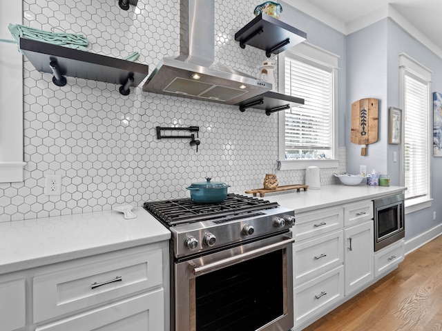 kitchen with tasteful backsplash, stainless steel appliances, wall chimney range hood, light hardwood / wood-style floors, and white cabinetry