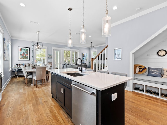 kitchen featuring an island with sink, light hardwood / wood-style flooring, decorative light fixtures, sink, and stainless steel dishwasher