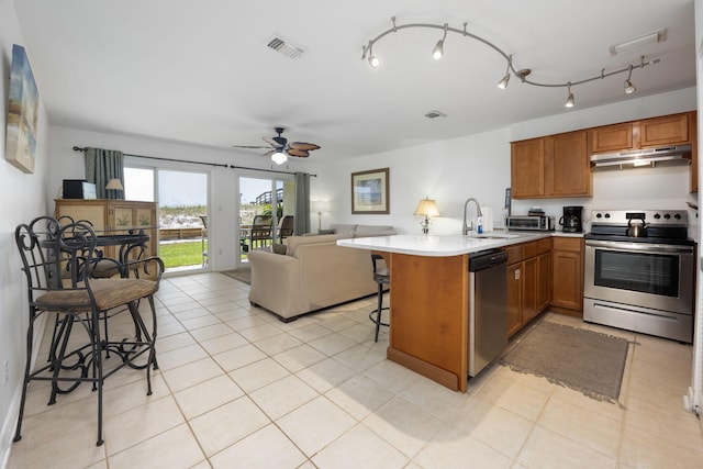 kitchen with under cabinet range hood, stainless steel appliances, a kitchen breakfast bar, open floor plan, and light countertops