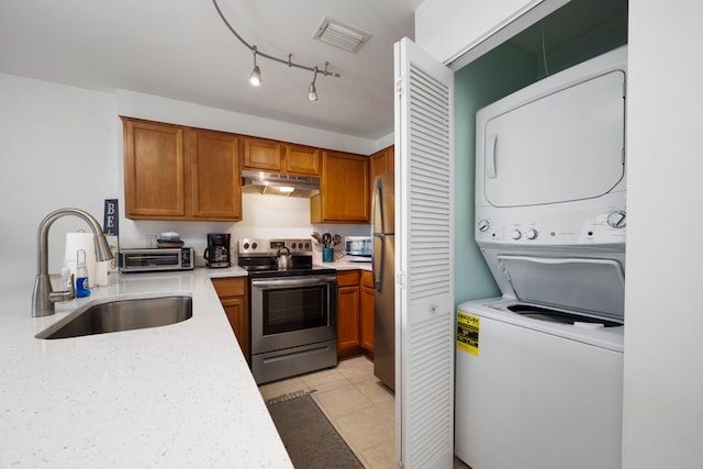 kitchen with under cabinet range hood, stainless steel appliances, a sink, light countertops, and stacked washer and clothes dryer