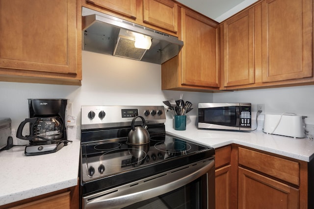 kitchen with stainless steel appliances, light stone counters, brown cabinets, and under cabinet range hood