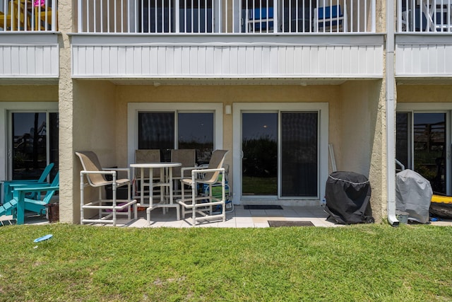 rear view of property featuring a patio area, a lawn, and stucco siding