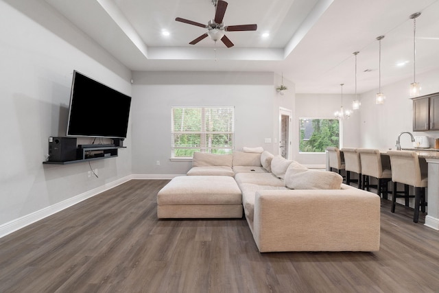 living area with recessed lighting, ceiling fan with notable chandelier, dark wood-style flooring, baseboards, and a tray ceiling