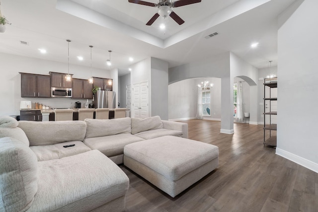 living room with baseboards, visible vents, arched walkways, a raised ceiling, and dark wood-style floors