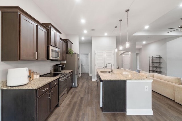 kitchen featuring visible vents, appliances with stainless steel finishes, open floor plan, dark brown cabinets, and a sink