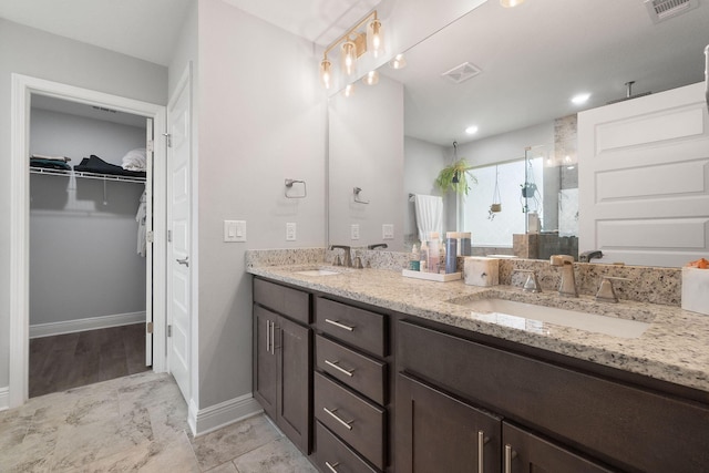 bathroom featuring double vanity, walk in shower, a sink, and visible vents