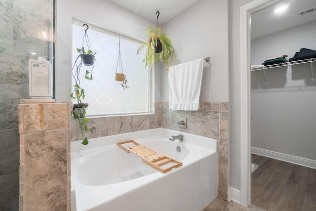 full bathroom with a spacious closet, visible vents, a bath, and wood finished floors