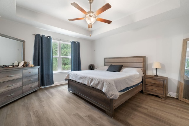 bedroom featuring wood finished floors, a raised ceiling, a ceiling fan, and baseboards