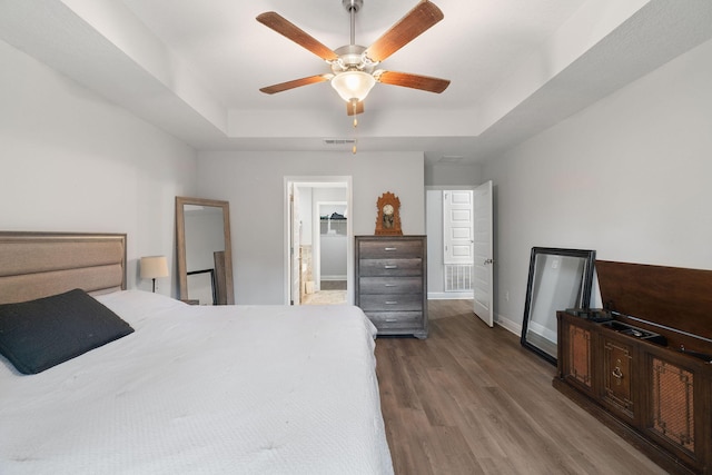 bedroom with baseboards, visible vents, ceiling fan, wood finished floors, and a tray ceiling