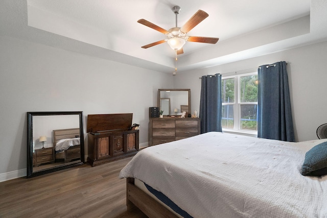 bedroom with a ceiling fan, baseboards, a raised ceiling, and wood finished floors