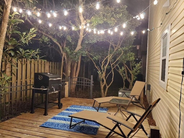 deck at night featuring grilling area and fence