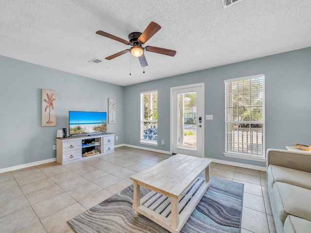 living room with ceiling fan, a textured ceiling, light tile patterned flooring, and a healthy amount of sunlight