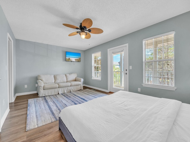 bedroom featuring ceiling fan, a textured ceiling, wood finished floors, access to outside, and baseboards