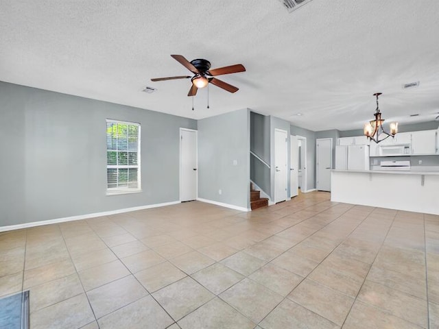 unfurnished living room featuring a textured ceiling, ceiling fan with notable chandelier, visible vents, baseboards, and stairway