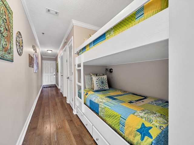 bedroom with a textured ceiling, dark wood-type flooring, visible vents, baseboards, and ornamental molding