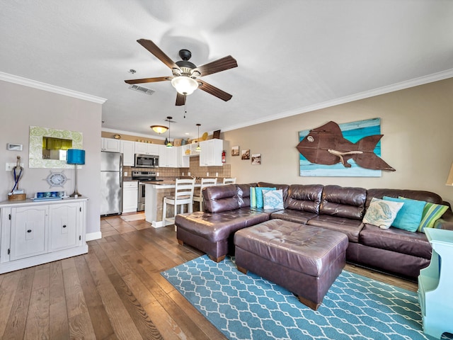 living room with ceiling fan, wood finished floors, visible vents, and crown molding