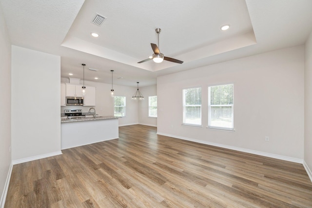 unfurnished living room featuring light wood-type flooring, a raised ceiling, plenty of natural light, and ceiling fan