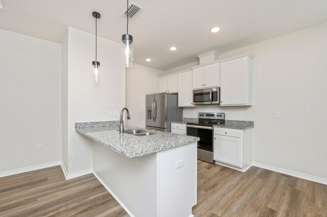 kitchen featuring stainless steel appliances, sink, light wood-type flooring, white cabinets, and hanging light fixtures