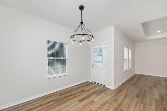 unfurnished dining area with a textured ceiling, a chandelier, and wood-type flooring