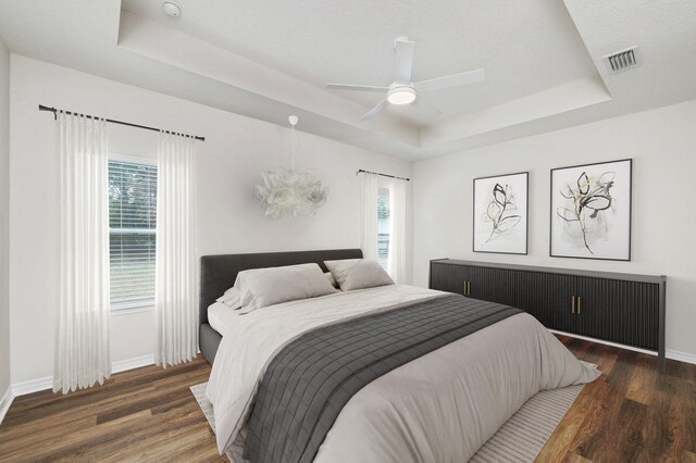 bedroom with ceiling fan, a tray ceiling, and dark hardwood / wood-style floors