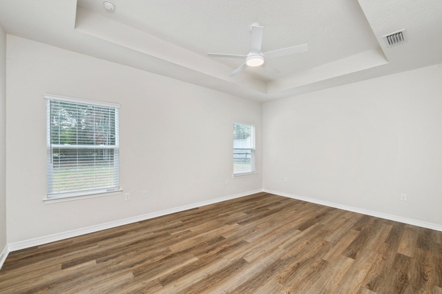 empty room with ceiling fan, hardwood / wood-style floors, and a raised ceiling