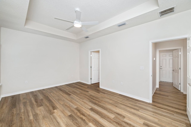 empty room featuring a tray ceiling, ceiling fan, a textured ceiling, and hardwood / wood-style flooring