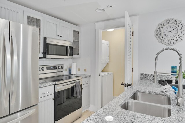 kitchen featuring decorative backsplash, white cabinetry, appliances with stainless steel finishes, stacked washer and dryer, and sink