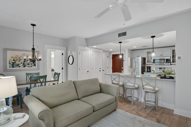 living room featuring ceiling fan with notable chandelier and light hardwood / wood-style flooring