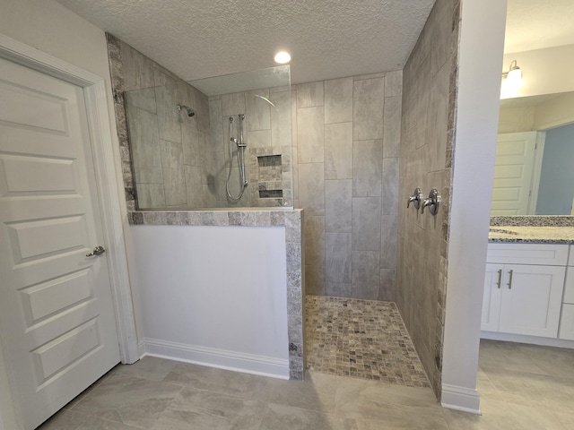 bathroom featuring a textured ceiling, a tile shower, and vanity