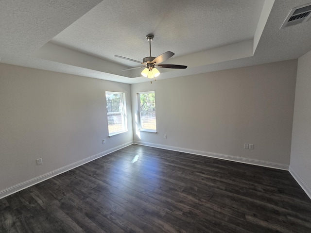 empty room featuring a textured ceiling, a tray ceiling, and dark hardwood / wood-style floors