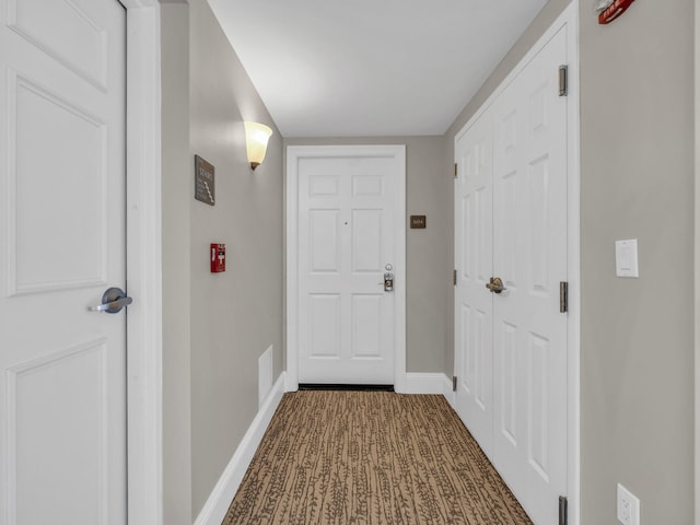 doorway featuring baseboards and dark carpet