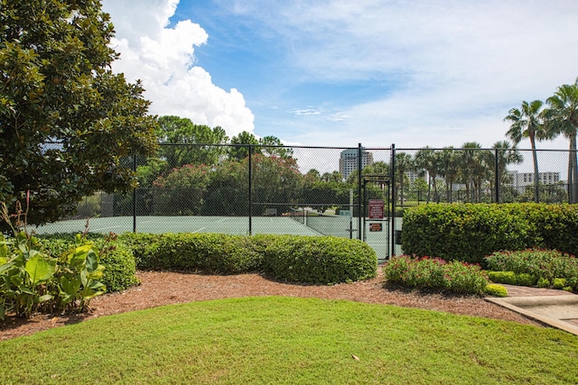 view of tennis court featuring a lawn, fence, and a gate