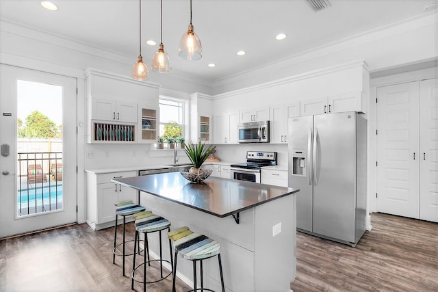 kitchen featuring crown molding, wood finished floors, a breakfast bar, appliances with stainless steel finishes, and a center island