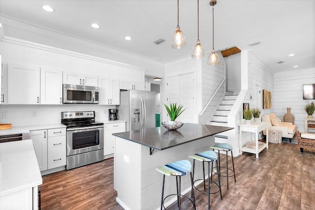 kitchen with a kitchen bar, dark wood-style flooring, ornamental molding, visible vents, and appliances with stainless steel finishes