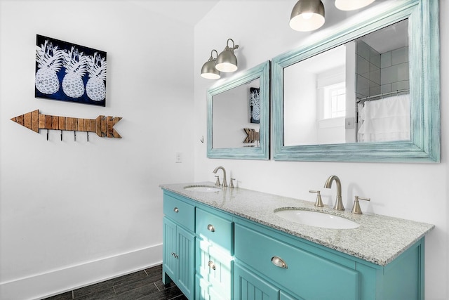 full bath featuring double vanity, a sink, baseboards, and wood tiled floor