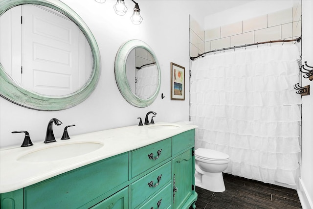 bathroom with toilet, wood finished floors, double vanity, and a sink