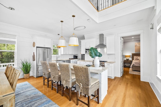 kitchen featuring wall chimney exhaust hood, appliances with stainless steel finishes, a breakfast bar area, and white cabinetry