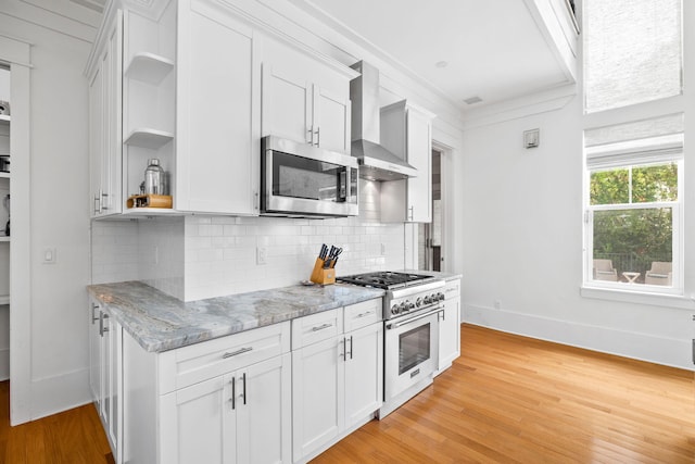 kitchen with open shelves, decorative backsplash, appliances with stainless steel finishes, wall chimney range hood, and light wood-type flooring