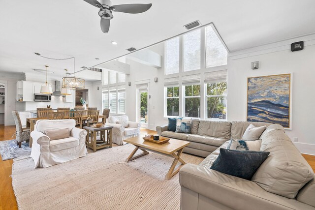 living room with ceiling fan, light hardwood / wood-style floors, and a towering ceiling