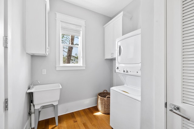 washroom with light wood-type flooring, stacked washer / dryer, cabinet space, and baseboards