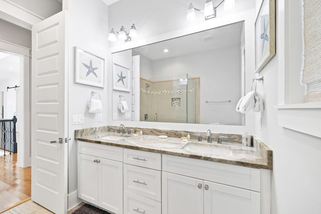 bathroom with double vanity, a sink, a shower stall, and wood finished floors