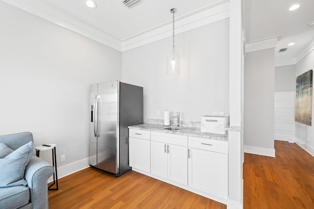 kitchen with light stone countertops, stainless steel fridge, ornamental molding, and light wood-style flooring