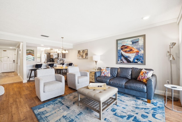 living room with wood-type flooring, a notable chandelier, and ornamental molding