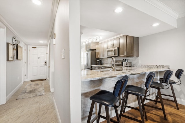 kitchen with ornamental molding, appliances with stainless steel finishes, light stone counters, tasteful backsplash, and a breakfast bar area