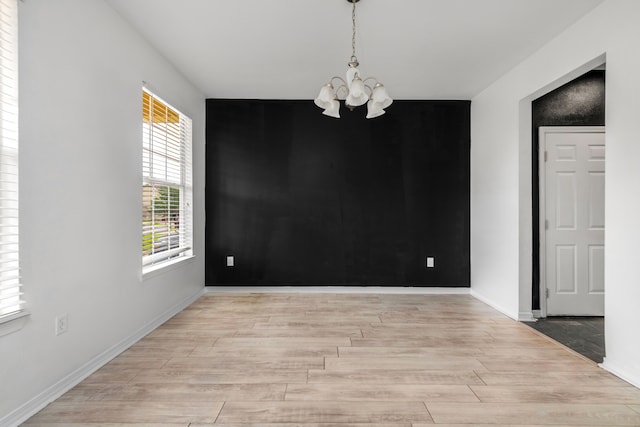 empty room with light hardwood / wood-style flooring, a notable chandelier, and plenty of natural light