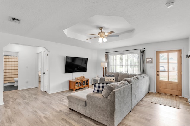 living room with ceiling fan, light wood-type flooring, a textured ceiling, and a tray ceiling