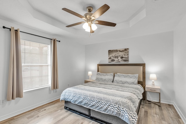 bedroom with a tray ceiling, ceiling fan, multiple windows, and light wood-type flooring