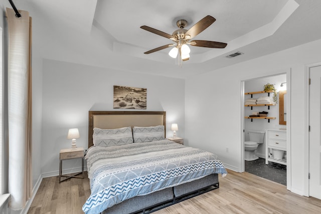 bedroom with light tile patterned floors, connected bathroom, ceiling fan, and a tray ceiling