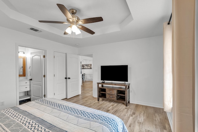 bedroom featuring ceiling fan, connected bathroom, a tray ceiling, and light hardwood / wood-style floors